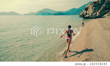 Aerial slow motion shot of a beautiful mom and her daughter running along the beach. Turkish Mediterranean coast Aerial slow motion shot of a beautiful mom and her daughter running along the beach. Turkish Mediterranean coast 102539245