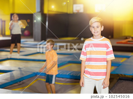 Smiling preteen boy posing in trampoline arena in amusement park 102545016