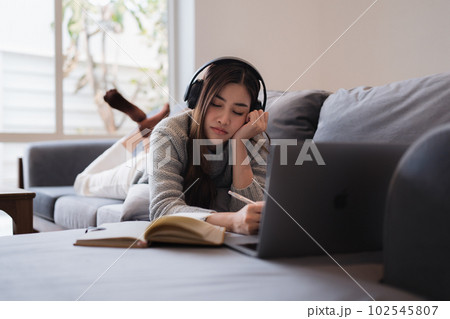 Online education, e-learning. Asian woman in stylish casual clothes, studying using a laptop, listening to online lecture, taking notes, online study at home Online education, e-learning. Asian woman in stylish casual clothes, studying using a laptop, listening to online lecture, taking notes, online study at home 102545807