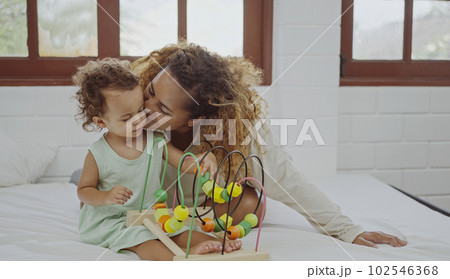 Happy mother and daughter playing with a toy developing colorful wooden blocks on bed together at home. Happy mother and daughter playing with a toy developing colorful wooden blocks on bed together at home. 102546368