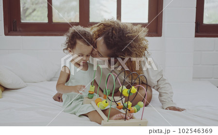 Happy mother and daughter playing with a toy developing colorful wooden blocks on bed together at home. 102546369