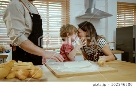 Father and mother teaching baby son kneading dough on kitchen counter at home. Parents and boy kid enjoy and fun indoors activity cooking together. 102546506