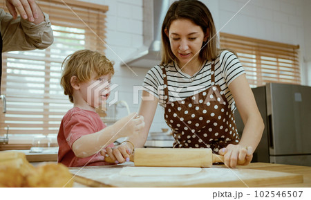 Father and mother teaching baby son kneading dough on kitchen counter at home. Parents and boy kid enjoy and fun indoors activity cooking together. 102546507