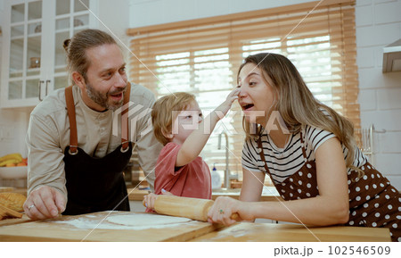Father and mother teaching baby son kneading dough on kitchen counter at home. Parents and boy kid enjoy and fun indoors activity cooking together. 102546509