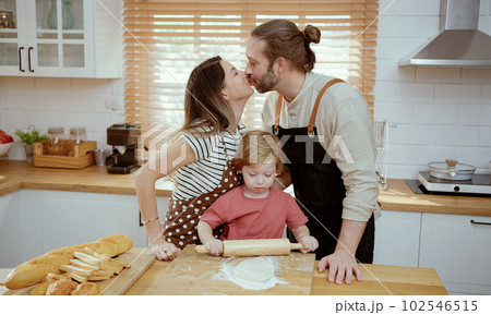 Father and mother teaching baby son kneading dough on kitchen counter at home. Parents and boy kid enjoy and fun indoors activity cooking together. 102546515