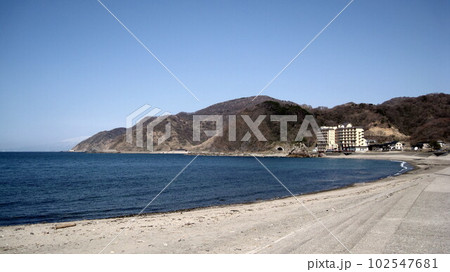 砂浜から見える日本海と荒倉山と由良温泉街と奥に雪積もった鳥海山 102547681