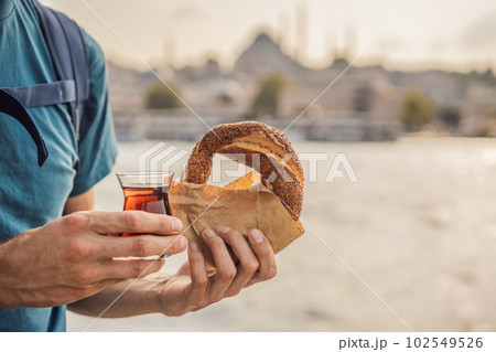 Man in Istanbul having breakfast with Simit and a glass of Turkish tea. Glass of Turkish tea and bagel Simit against golden horn bay and the Galata Tower in Istanbul, Turkey. Turkiye Man in Istanbul having breakfast with Simit and a glass of Turkish tea. Glass of Turkish tea and bagel Simit against golden horn bay and the Galata Tower in Istanbul, Turkey. Turkiye 102549526