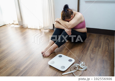 Obese Woman with fat upset bored of dieting Weight loss fail  Fat diet and scale sad asian woman on weight scale at home weight control. 102556986