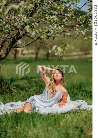 woman sleeps on a white bed in the fresh spring grass in the garden. Dressed in a blue nightgown. 102565583