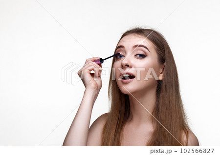 Beautiful young woman applying black mascara on long thick eyelashes Beautiful young woman applying black mascara on long thick eyelashes 102566827