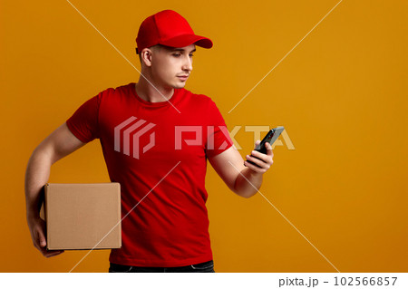 Delivery man employee in red cap, t-shirt holding empty cardboard box and phone 102566857