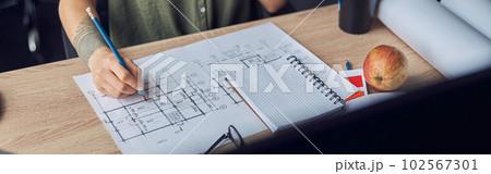 Close up shot of hand of female interior designer making notes on a blueprint, sitting at the table in her office Close up shot of hand of female interior designer making notes on a blueprint, sitting at the table in her office 102567301