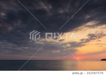 dramatic dawn at the sea. gray clouds on the sky with red sun above the horizon. summer holidays rainy weather forecast 102567570