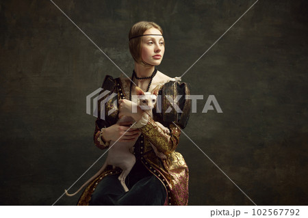 Portrait of beautiful young girl in elegant clothing over dark vintage background posing with sphynx cat. Lady with ermine remake 102567792