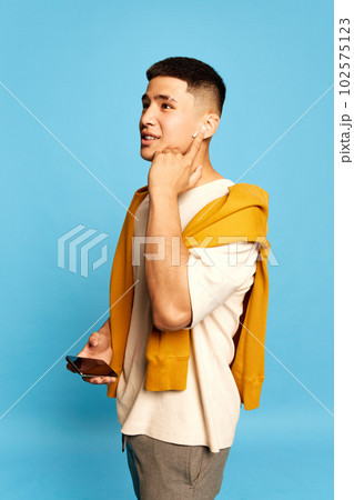 Portrait with one young attractive man, guy wearing casual style clothes listening to music via earpods over blue color studio background 102575123