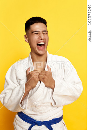 Close up portrait with winner, male taekwondo, karate athlete wearing white kimono relaxing after fight over yellow background 102575240