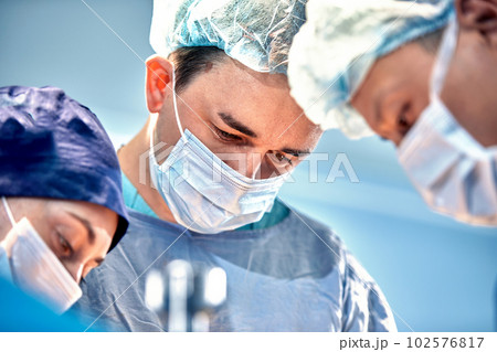 Close-up view of surgeons faces in medical masks during a complex and intense operation, doctors save the patient's life, teamwork of surgeons Close-up view of surgeons faces in medical masks during a complex and intense operation, doctors save the patient's life, teamwork of surgeons 102576817