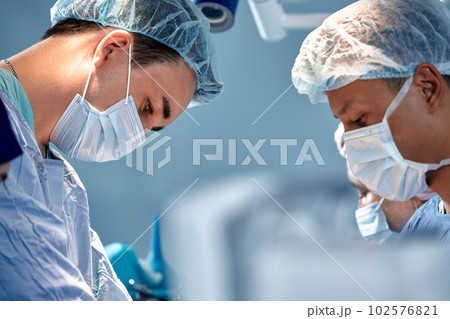 Close-up view of surgeons faces in medical masks during a complex and intense operation, doctors save the patient's life, teamwork of surgeons Close-up view of surgeons faces in medical masks during a complex and intense operation, doctors save the patient's life, teamwork of surgeons 102576821