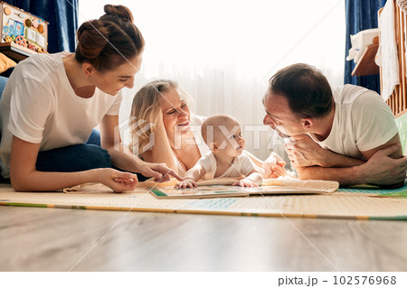 Parents together with their child play and study a children's book, lying on the floor in a bright children's room. Happy friendly family concept. Parents together with their child play and study a children's book, lying on the floor in a bright children's room. Happy friendly family concept. 102576968