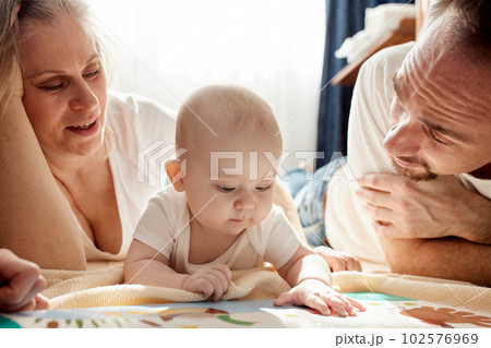 Close-up view of young parents, mom and dad, reading a children's book to their baby. Family training and education concept. Close-up. 102576969