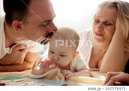 Close-up view of young parents, mom and dad, reading a children's book to their baby. Family training and education concept. Close-up. 102576971