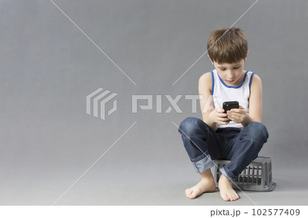 Child with a mobile phone. Schoolboy looks into the smartphone on a gray background Child with a mobile phone. Schoolboy looks into the smartphone on a gray background 102577409