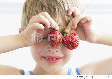 A child with strawberries. The boy holds two red berries near the eyes 102577823