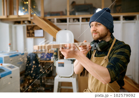 Young man carpenter blowing sawdust from board wooden plank 102579092