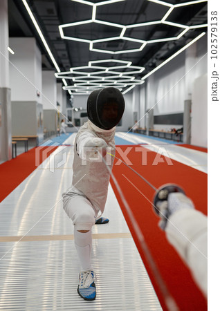 Swordsman standing in fencing lunge during training fight in fencer club 102579138