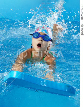 Little girl learning to swim in indoor pool with pool board 102579228