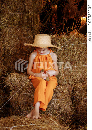 Child girl in an orange suit and a straw hat sits with a duck Child girl in an orange suit and a straw hat sits with a duck 102583136