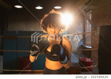 Outcry independent girl power. Angry african american woman fighter with boxing gloves looking serious aggressive standing on boxing ring. Strong powerful fighter girl training punches Outcry independent girl power. Angry african american woman fighter with boxing gloves looking serious aggressive standing on boxing ring. Strong powerful fighter girl training punches 102586626