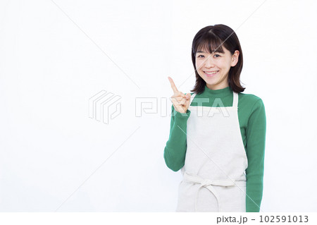 白い背景の前で人差し指を立てるエプロン姿の30代主婦 102591013