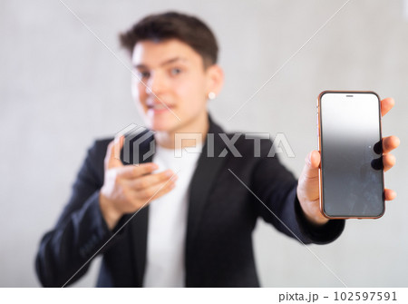 Unfocused agent in suit jacket shows dark empty mobile phone screen and points at device with hand Unfocused agent in suit jacket shows dark empty mobile phone screen and points at device with hand 102597591