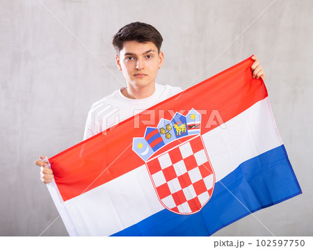 Calm young man holding flag of Croatia against unicoloured background Calm young man holding flag of Croatia against unicoloured background 102597750
