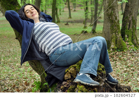Pregnant woman relaxing on a tree trunk Pregnant woman relaxing on a tree trunk 102604527