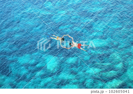 Drone view of couple snorkeling in clear blue sea water Drone view of couple snorkeling in clear blue sea water 102605041