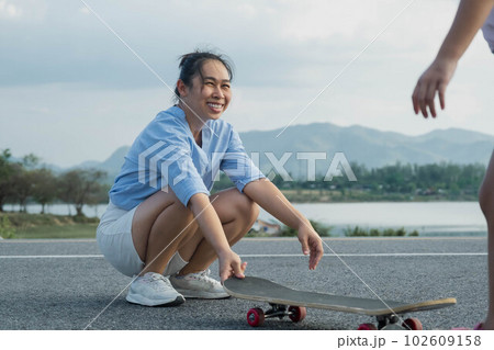 Mother teaching her daughter how to skateboard in the park. Child riding skate board. Healthy sports and outdoor activities for school children in the summer. 102609158