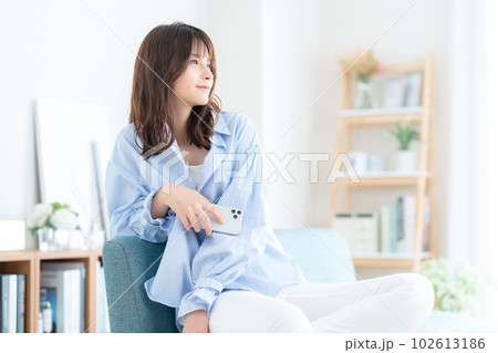 リビングのソファでスマホを操作する若い女性 102613186