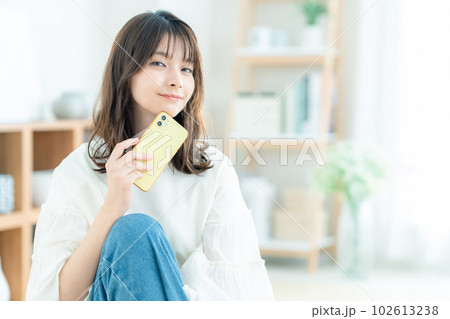リビングで座ってスマホを操作する若い女性 リビングで座ってスマホを操作する若い女性 102613238