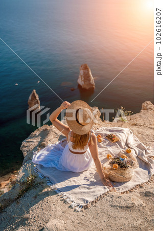 woman sea trevel. photo of a beautiful woman with long blond hair in a pink shirt and denim shorts and a hat having a picnic on a hill overlooking the sea 102616207