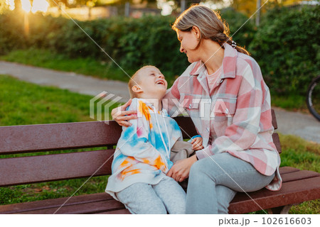 mother and son sit on a park bench in the rays of the setting sun. the concept of a family. Mother's Day. beautiful girl (mother) with a boy (son) in the park in the park are sitting on a bench at 102616603