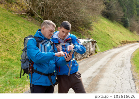 Two hikers are in the mountains in the spring nature outdoor. Hiking with backpacks. Two friends travel together in picturesque places. The man shows the way. Two men on a hiking trip in the mountains 102616626