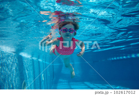 Cute, funny, little baby girl, toddler in pink swimsuit and goggles swimming underwater in swimming pool. Water sports activity 102617012