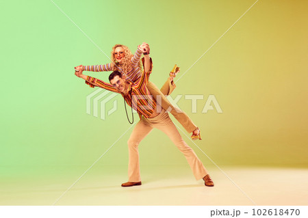 Cheerful, positive, smiling couple, man and woman in vintage clothes dancing disco dance against gradient green yellow background Cheerful, positive, smiling couple, man and woman in vintage clothes dancing disco dance against gradient green yellow background 102618470