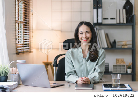 Portrait of a young, cheerful, happy, positive, cute, and beautiful Asian millennial businesswoman Working on Financial and Marketing Projects while sitting indoors in a home office. 102619622