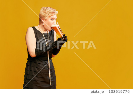 Portrait with lady, woman wearing black vintage dress holding big beer mug and drinking with pleasure over yellow background Portrait with lady, woman wearing black vintage dress holding big beer mug and drinking with pleasure over yellow background 102619776