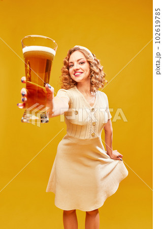 Young, sexy girl, Oktoberfest waitress wearing vintage dress holding beer glass and serving over yellow background. Alcohol degustation Young, sexy girl, Oktoberfest waitress wearing vintage dress holding beer glass and serving over yellow background. Alcohol degustation 102619785