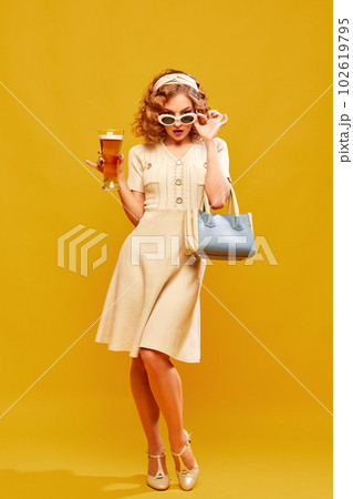 Young, sexy girl wearing vintage clothes and sunglasses holding lager beer glass over yellow studio background. Concept of drinks, alcohol, degustation Young, sexy girl wearing vintage clothes and sunglasses holding lager beer glass over yellow studio background. Concept of drinks, alcohol, degustation 102619795