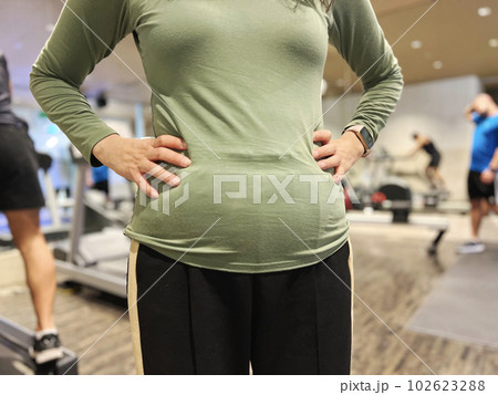 フィットネスジムで両手を腰にあててぽっこりお腹の女性 102623288